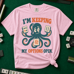 I'm Keeping My Options Open T-Shirt in Blossom, knotted flat lay on a green mahjong mat - worried teal octopus holding a dot tile, a bam tile, and a green dragon tile - "I'M KEEPING MY OPTIONS OPEN." in teal and orange retro letters