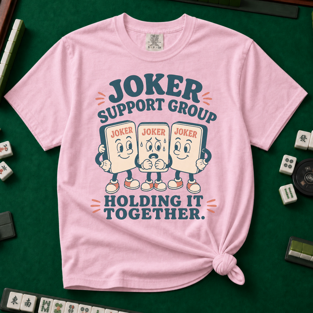 Joker Support Group Holding It Together T-Shirt in Blossom, knotted flat lay on a green mahjong mat - three retro cartoon joker tiles in sneakers, the middle one sweating nervously while the other two hold him up - "JOKER SUPPORT GROUP - HOLDING IT TOGETHER." in teal retro letters