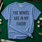 The Winds Are In My Favor T-Shirt in Blue Jean, knotted flat lay on a green mahjong mat - "THE WINDS ARE IN MY FAVOR" in tall black letters