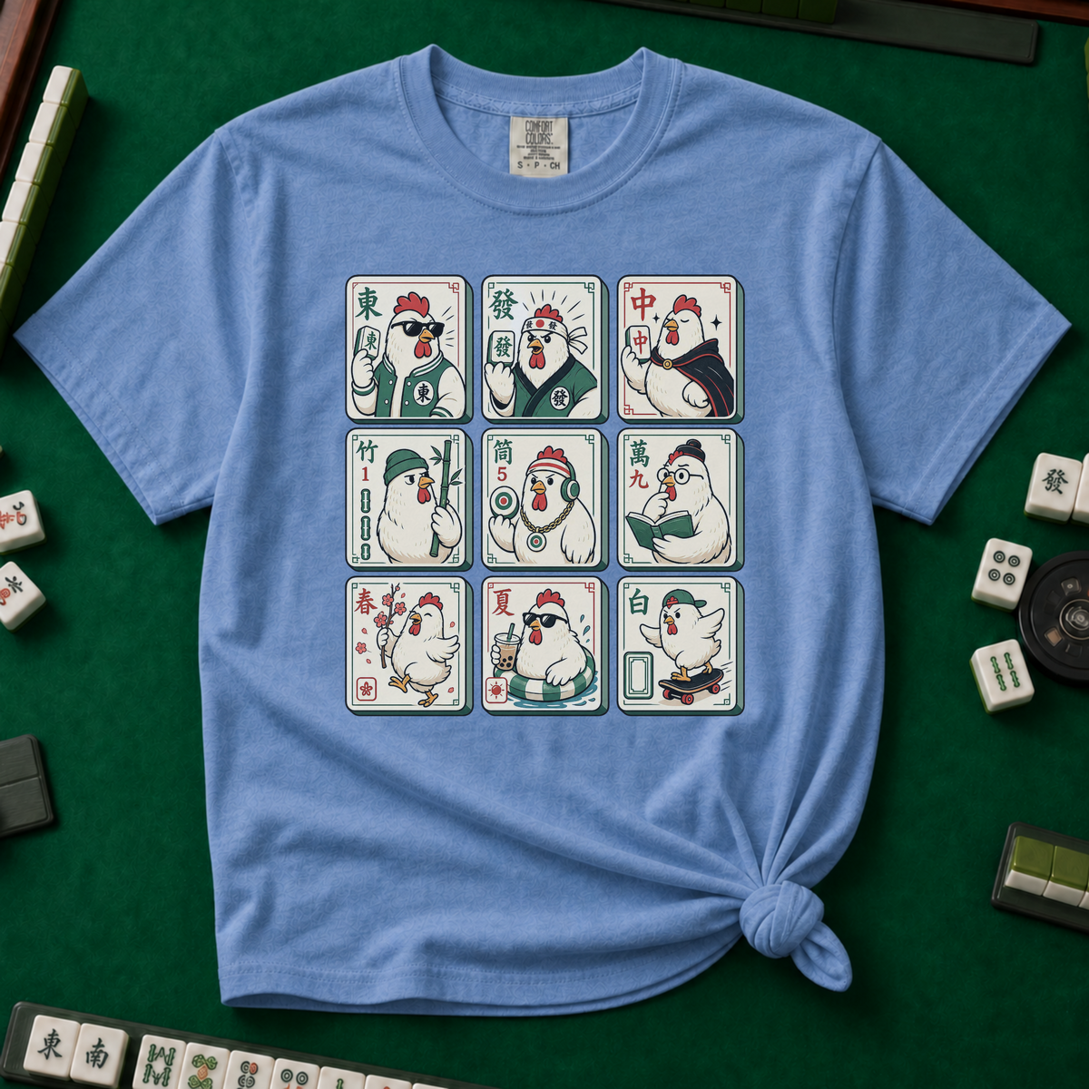 Mahjong Chicken Tiles T-Shirt in Blue Jean, knotted flat lay on a green mahjong mat - a 3x3 grid of mahjong tiles, each starring a cartoon chicken with its own personality - varsity jacket, karate gi, cape, beanie, headphones, bookworm glasses, cherry blossom, pool floatie and skateboard