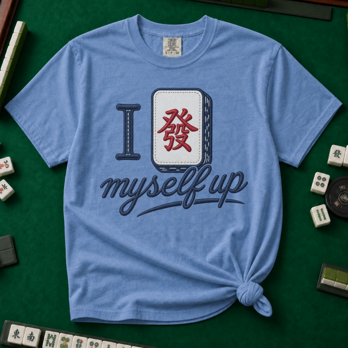 I Set Myself Up T-Shirt in Blue Jean, knotted flat lay on a green mahjong mat - a stitched-look varsity rebus - a navy letter I beside a cream fa dragon tile with the red character, over "myself up" in navy script