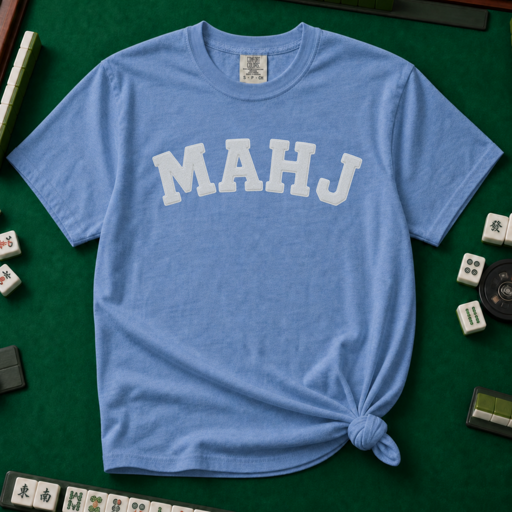MAHJ Varsity T-Shirt in Blue Jean, knotted flat lay on a green mahjong mat - "MAHJ" in big white varsity arch letters with a stitched letterman look
