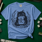 Linocut Tile Cat T-Shirt in Blue Jean, knotted flat lay on a green mahjong mat - a linocut-style black cat hugging a Green Dragon mahjong tile inside a wreath of wheat, daisies and lavender