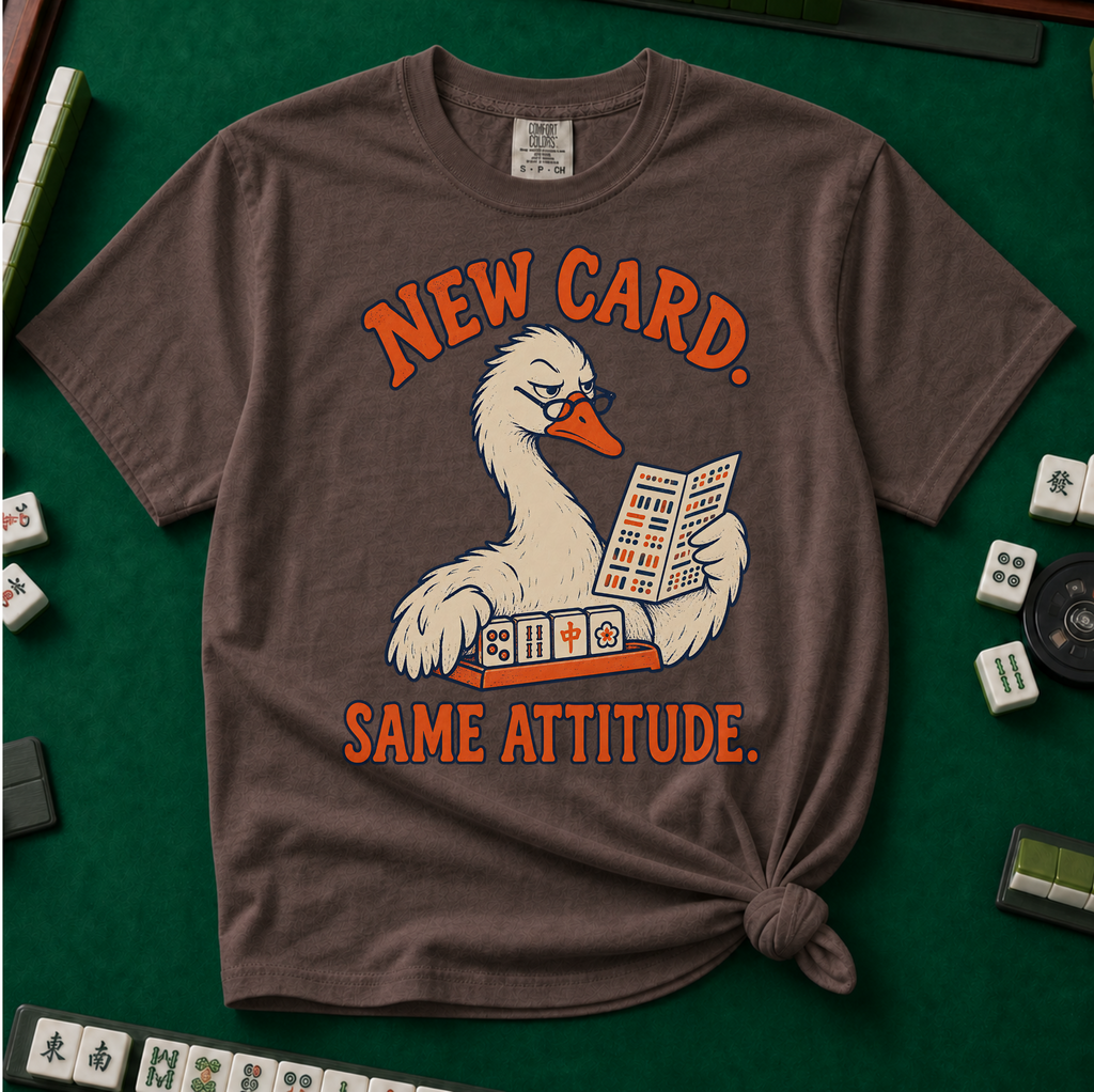 New Card T-Shirt in Espresso - knotted tee flat lay on a green mahjong mat with tiles, printed with a white goose in glasses reading the new mahjong card over a rack of tiles, with the words NEW CARD. SAME ATTITUDE.