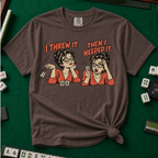 I Threw It Then I Needed It T-Shirt in Espresso, knotted flat lay on a green mahjong mat - a retro comic two-panel scene of a woman smugly flicking away a mahjong tile, then panicking when she needs it, with the words "I THREW IT. THEN I NEEDED IT."