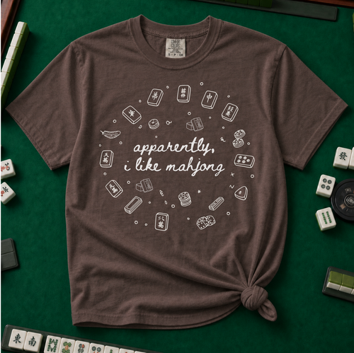 Apparently I like Mahjong T-Shirt in Espresso - knotted tee on a green mahjong mat with scattered tiles, printed with four line-art mahjong tiles and the words Apparently I Like Mahjong in script