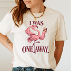 I Was One Away T-Shirt in Ivory - worn by a model outdoors, printed with a pink flamingo standing on one leg and holding a mahjong tile, with the words I WAS ONE AWAY.