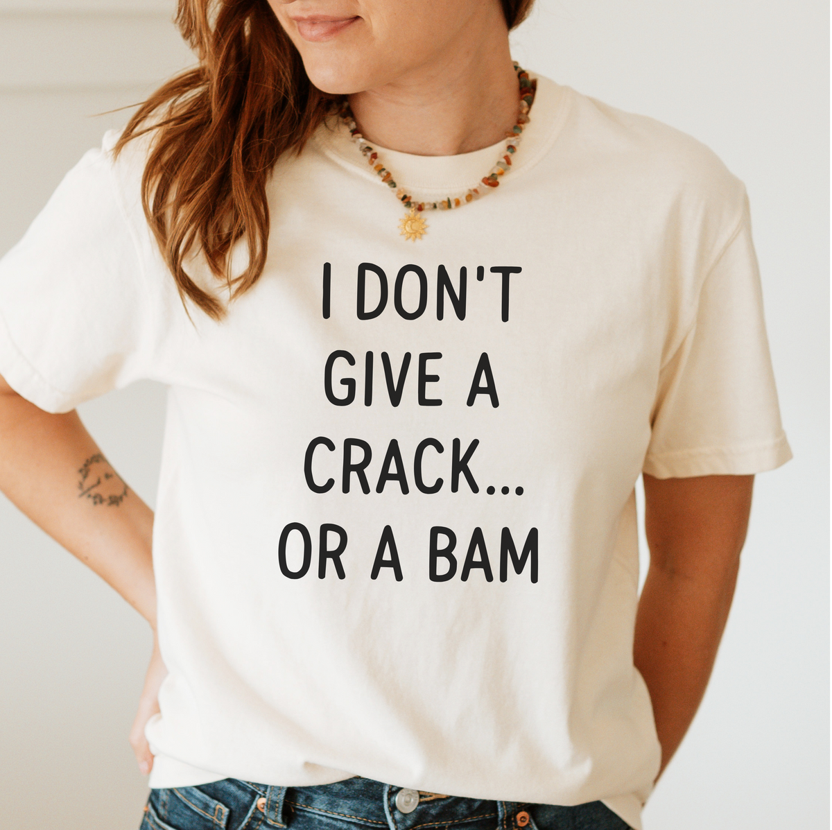 Woman wearing the I Don't Give A Crack Or A Bam T-Shirt in Ivory - "I DON'T GIVE A CRACK... OR A BAM" in black handwritten-style letters