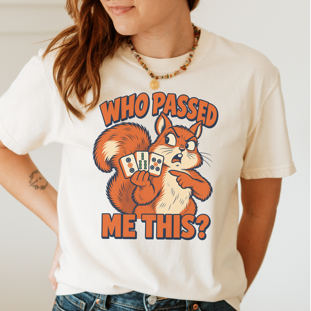 Woman wearing the Who Passed Me This T-Shirt in Ivory - retro orange squirrel holding three mahjong tiles, pointing an accusing paw - "WHO PASSED ME THIS?" in bold orange letters