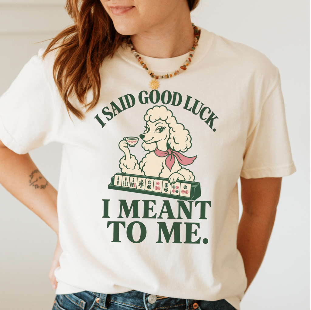 I Said Good Luck T-Shirt in Ivory - worn by a model, printed with a cream poodle in a pink scarf holding a teacup behind a rack of mahjong tiles, with the words I SAID GOOD LUCK. I MEANT TO ME.