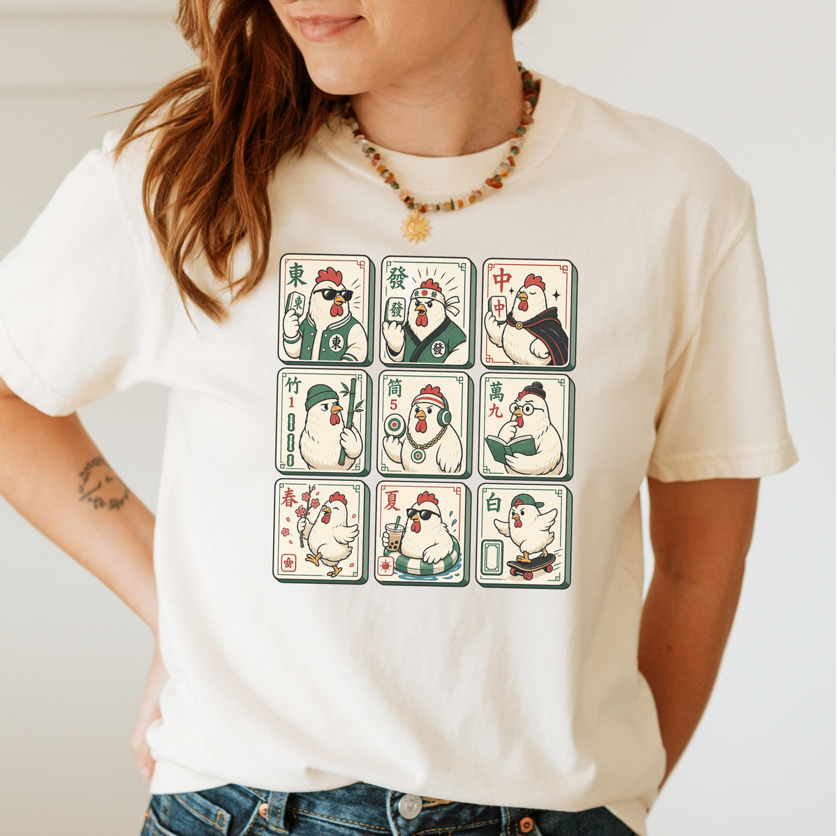 Woman wearing the Mahjong Chicken Tiles T-Shirt in Ivory - a 3x3 grid of mahjong tiles, each starring a cartoon chicken with its own personality - varsity jacket, karate gi, cape, beanie, headphones, bookworm glasses, cherry blossom, pool floatie and skateboard