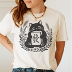 Woman wearing the Linocut Tile Cat T-Shirt in Ivory - a linocut-style black cat hugging a Green Dragon mahjong tile inside a wreath of wheat, daisies and lavender