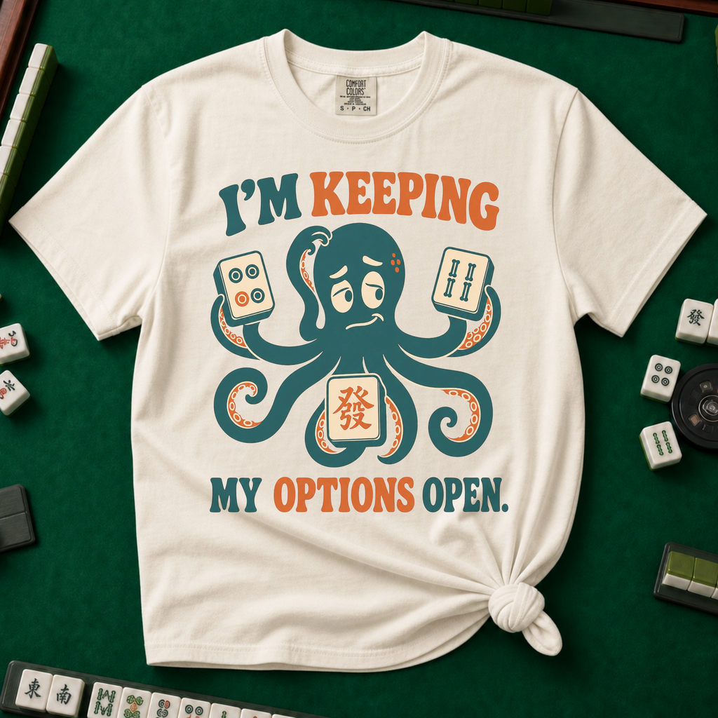 I'm Keeping My Options Open T-Shirt in Ivory, knotted flat lay on a green mahjong mat - worried teal octopus holding a dot tile, a bam tile, and a green dragon tile - "I'M KEEPING MY OPTIONS OPEN." in teal and orange retro letters
