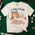 I Had A Plan Before The Charleston T-Shirt in Ivory, knotted flat lay on a green mahjong mat - a stressed cartoon fox with glasses and a strategy sketch being handed three mahjong tiles, with the words "I HAD A PLAN BEFORE THE CHARLESTON."
