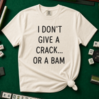 I Don't Give A Crack Or A Bam T-Shirt in Ivory, knotted flat lay on a green mahjong mat - "I DON'T GIVE A CRACK... OR A BAM" in black handwritten-style letters