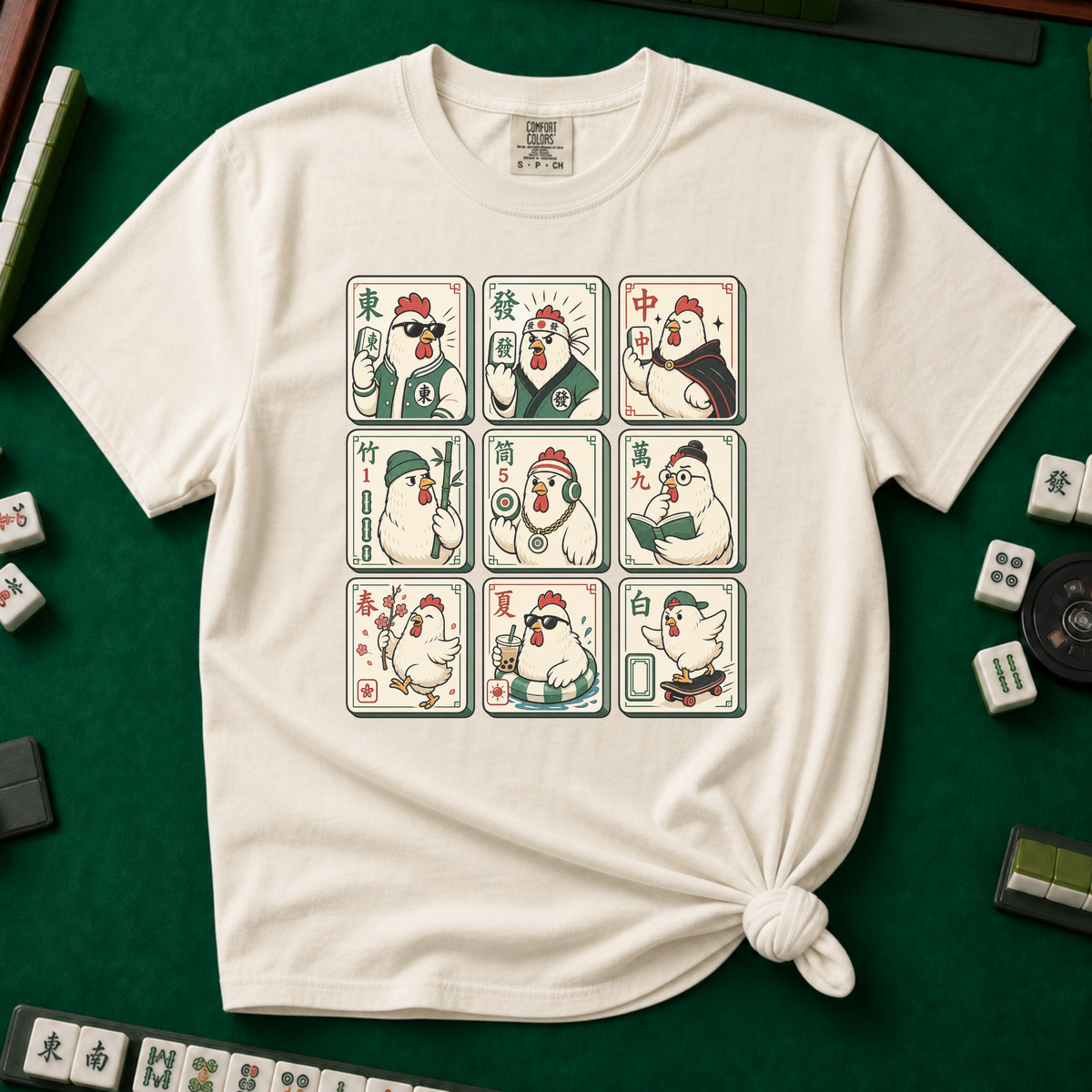 Mahjong Chicken Tiles T-Shirt in Ivory, knotted flat lay on a green mahjong mat - a 3x3 grid of mahjong tiles, each starring a cartoon chicken with its own personality - varsity jacket, karate gi, cape, beanie, headphones, bookworm glasses, cherry blossom, pool floatie and skateboard