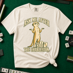 Ask Me After The Charleston T-Shirt in Ivory, knotted flat lay on a green mahjong mat - shrugging meerkat standing beside three mahjong tiles - "ASK ME AFTER THE CHARLESTON." in cream collegiate letters