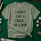 I Don't Give A Crack Or A Bam T-Shirt in Moss, knotted flat lay on a green mahjong mat - "I DON'T GIVE A CRACK... OR A BAM" in black handwritten-style letters
