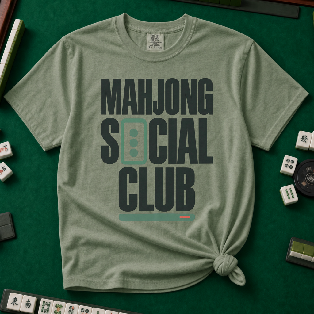 Mahjong Social Club Bold T-Shirt in Moss, knotted flat lay on a green mahjong mat - bold charcoal block letters "MAHJONG SOCIAL CLUB" with a green three-dot tile as the O in SOCIAL and a green pusher bar underline