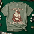 I Can't Pass These I Love Them T-Shirt in Moss, knotted flat lay on a green mahjong mat - lovestruck otter hugging three mahjong tiles to her chest - "I CAN'T PASS THESE. I LOVE THEM." in cream retro letters