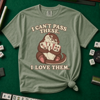 I Can't Pass These I Love Them T-Shirt in Moss, knotted flat lay on a green mahjong mat - lovestruck otter hugging three mahjong tiles to her chest - "I CAN'T PASS THESE. I LOVE THEM." in cream retro letters