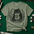 Linocut Tile Cat T-Shirt in Moss, knotted flat lay on a green mahjong mat - a linocut-style black cat hugging a Green Dragon mahjong tile inside a wreath of wheat, daisies and lavender