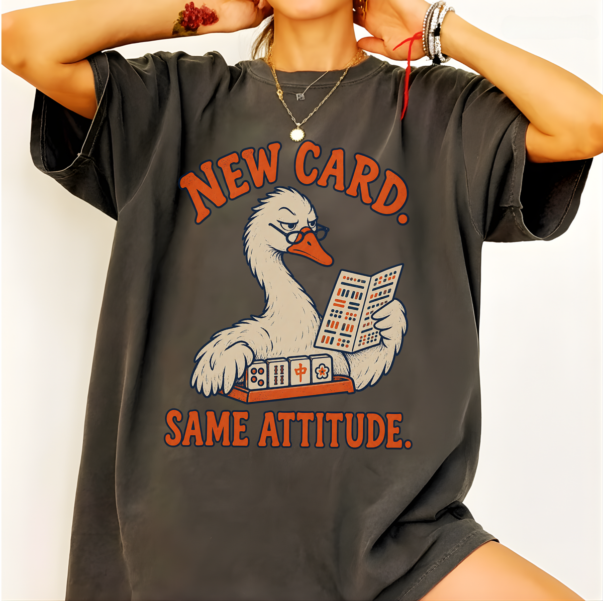 New Card T-Shirt in Pepper - worn oversized by a model, printed with a white goose in glasses reading the new mahjong card over a rack of tiles, with the words NEW CARD. SAME ATTITUDE.