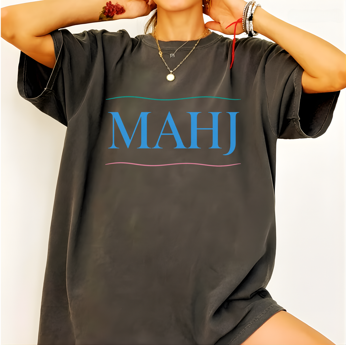 Woman wearing the MAHJ Wave T-Shirt in Pepper, oversized fit - "MAHJ" in sky-blue serif letters between a teal wave line above and a pink wave line below