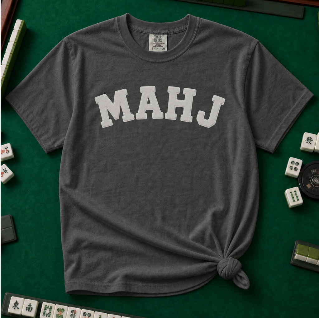 MAHJ Varsity T-Shirt in Pepper, knotted flat lay on a green mahjong mat - "MAHJ" in big white varsity arch letters with a stitched letterman look
