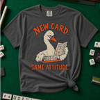 New Card T-Shirt in Pepper - knotted tee flat lay on a green mahjong mat with tiles, printed with a white goose in glasses reading the new mahjong card over a rack of tiles, with the words NEW CARD. SAME ATTITUDE.