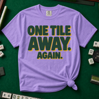 One Tile Away Again T-Shirt in Violet, knotted flat lay on a green mahjong mat - "ONE TILE AWAY. AGAIN." in bold deep-green block letters with a gold drop shadow