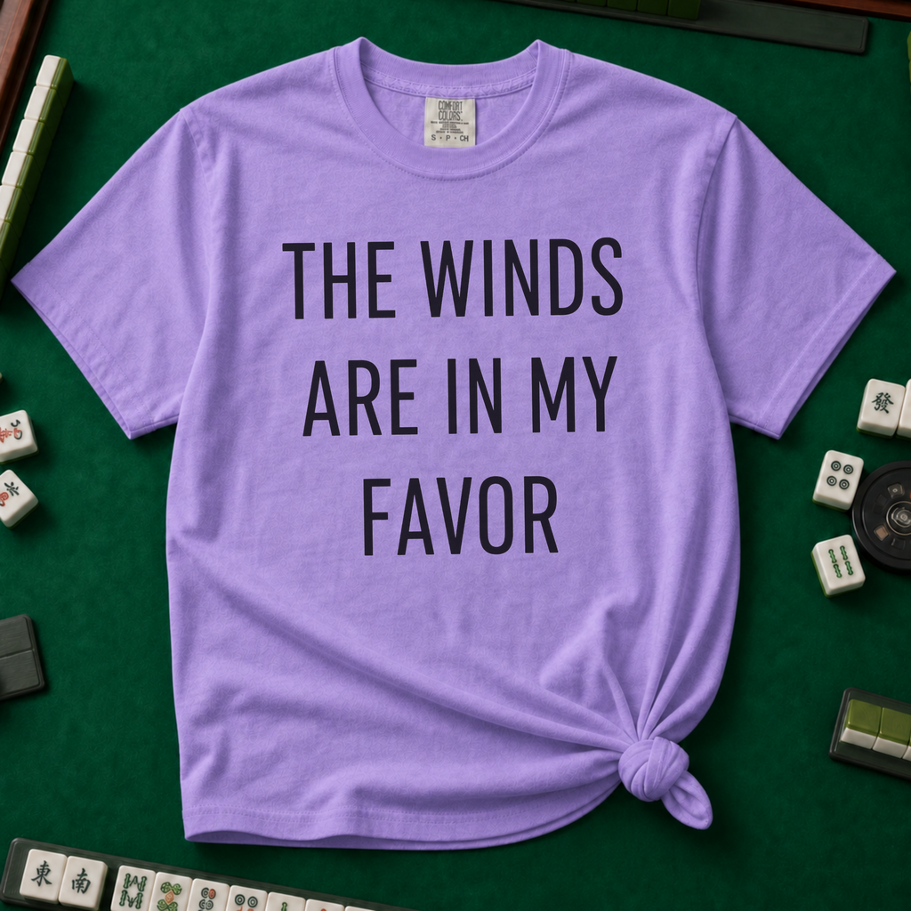 The Winds Are In My Favor T-Shirt in Violet, knotted flat lay on a green mahjong mat - "THE WINDS ARE IN MY FAVOR" in tall black letters