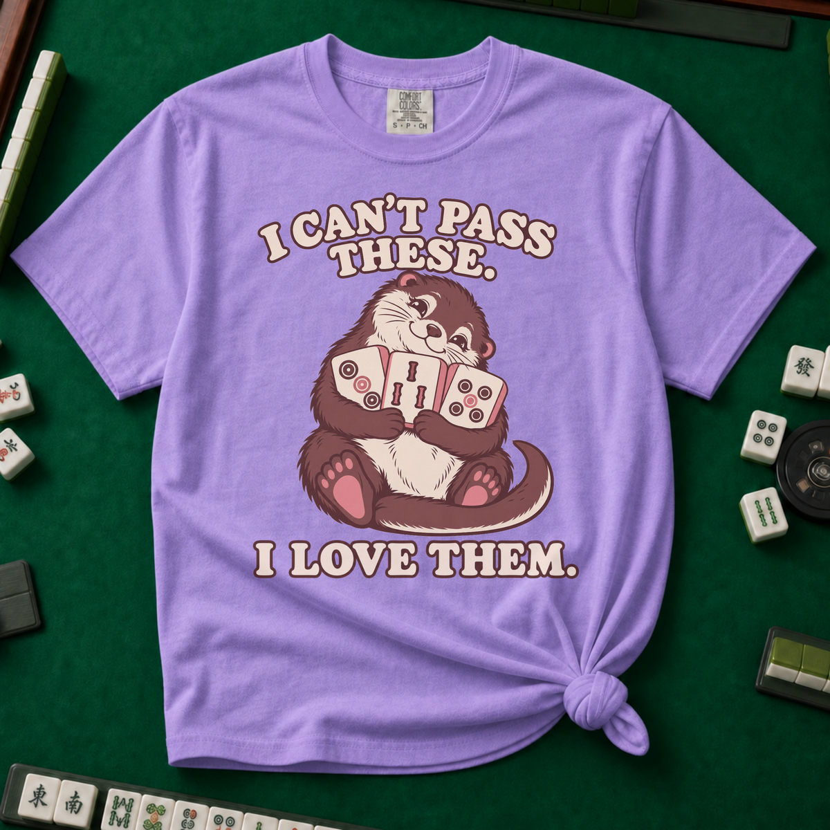 I Can't Pass These I Love Them T-Shirt in Violet, knotted flat lay on a green mahjong mat - lovestruck otter hugging three mahjong tiles to her chest - "I CAN'T PASS THESE. I LOVE THEM." in cream retro letters