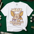 Wait What Did You Throw T-Shirt in White, knotted flat lay on a green mahjong mat - a wide-eyed fluffy bat with huge golden ears leaning in over a fallen dot tile - "WAIT. WHAT DID YOU THROW?" in cream bubble letters