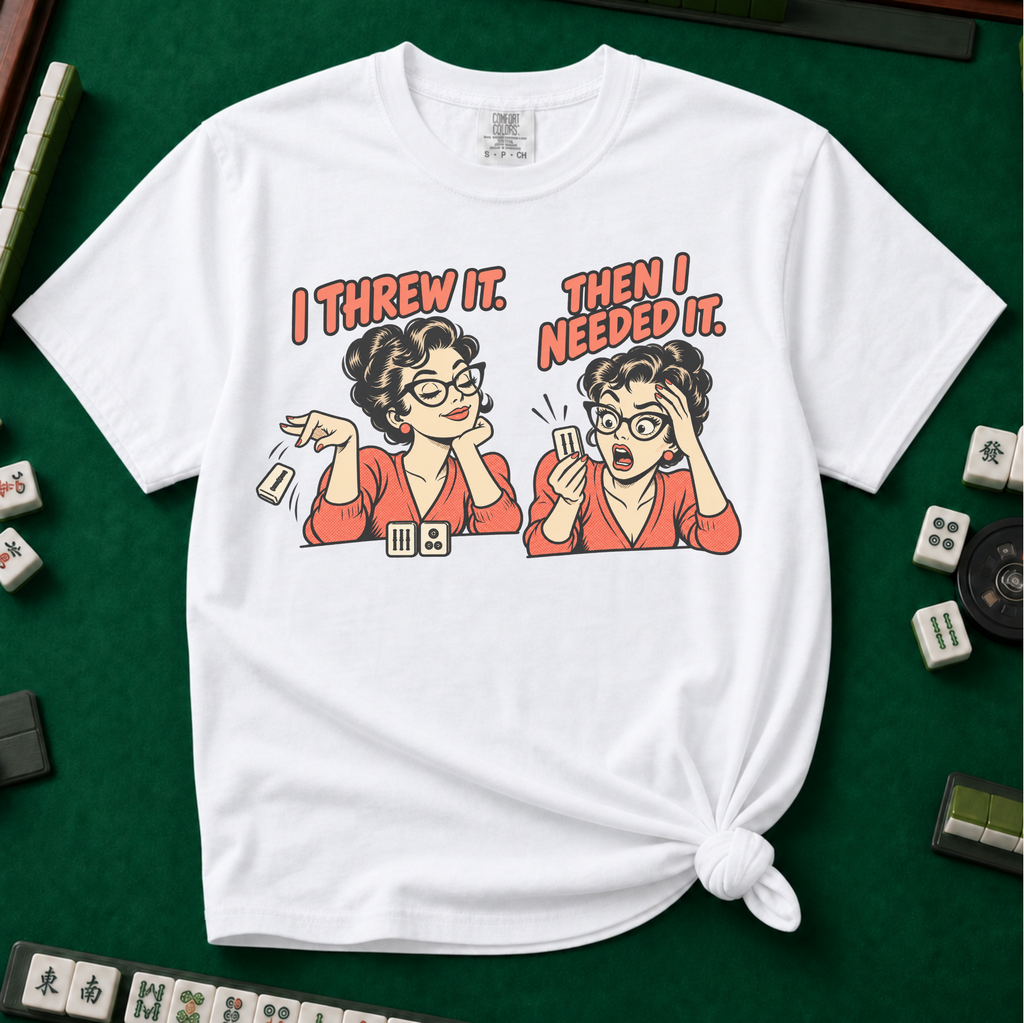 I Threw It Then I Needed It T-Shirt in White, knotted flat lay on a green mahjong mat - a retro comic two-panel scene of a woman smugly flicking away a mahjong tile, then panicking when she needs it, with the words "I THREW IT. THEN I NEEDED IT."