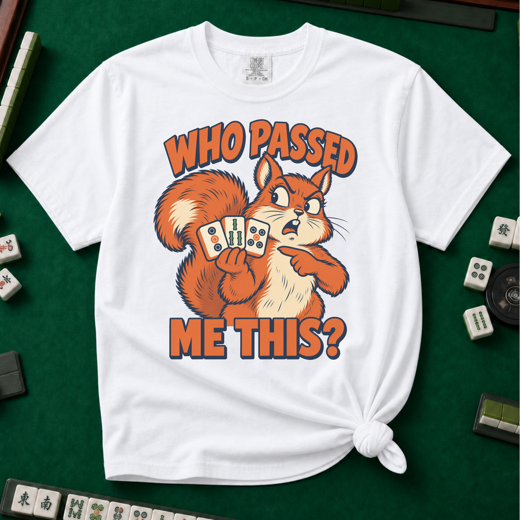 Who Passed Me This T-Shirt in White, knotted flat lay on a green mahjong mat - retro orange squirrel holding three mahjong tiles, pointing an accusing paw - "WHO PASSED ME THIS?" in bold orange letters