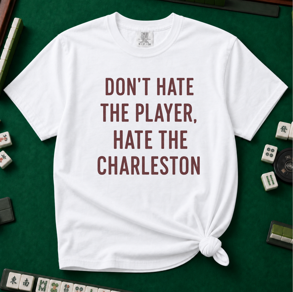 Don't Hate The Player Hate The Charleston T-Shirt in White, knotted flat lay on a green mahjong mat - "DON'T HATE THE PLAYER, HATE THE CHARLESTON" in deep burgundy block letters