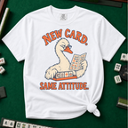 New Card T-Shirt in White - knotted tee flat lay on a green mahjong mat with tiles, printed with a white goose in glasses reading the new mahjong card over a rack of tiles, with the words NEW CARD. SAME ATTITUDE.