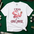 I Was One Away T-Shirt in White - knotted tee flat lay on a green mahjong mat with tiles, printed with a pink flamingo standing on one leg and holding a mahjong tile, with the words I WAS ONE AWAY.