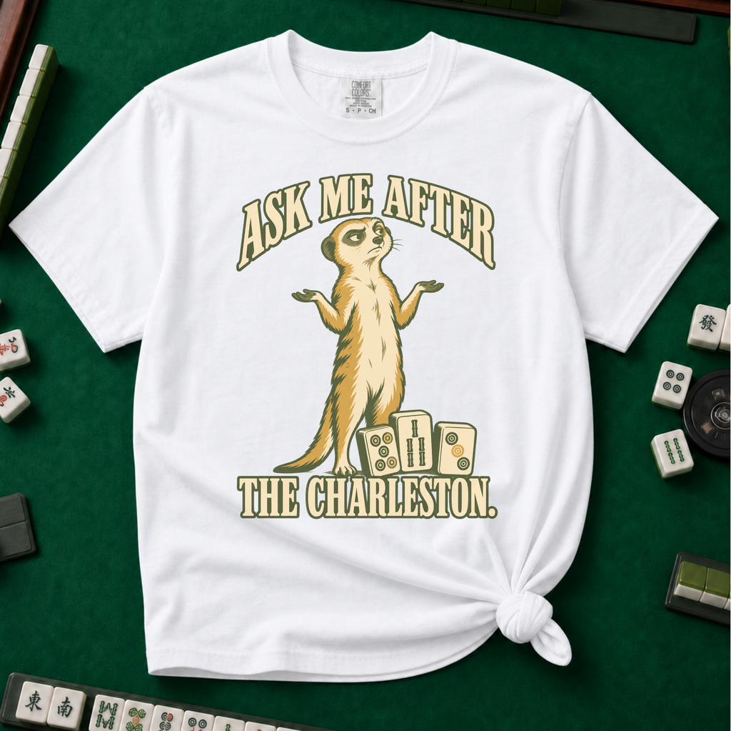 Ask Me After The Charleston T-Shirt in White, knotted flat lay on a green mahjong mat - shrugging meerkat standing beside three mahjong tiles - "ASK ME AFTER THE CHARLESTON." in cream collegiate letters