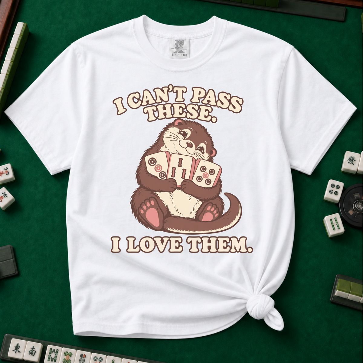 I Can't Pass These I Love Them T-Shirt in White, knotted flat lay on a green mahjong mat - lovestruck otter hugging three mahjong tiles to her chest - "I CAN'T PASS THESE. I LOVE THEM." in cream retro letters