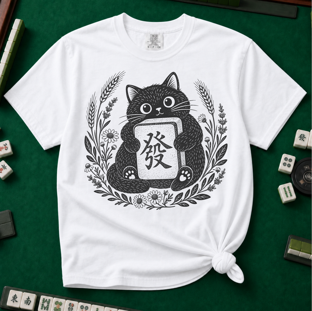Linocut Tile Cat T-Shirt in White, knotted flat lay on a green mahjong mat - a linocut-style black cat hugging a Green Dragon mahjong tile inside a wreath of wheat, daisies and lavender
