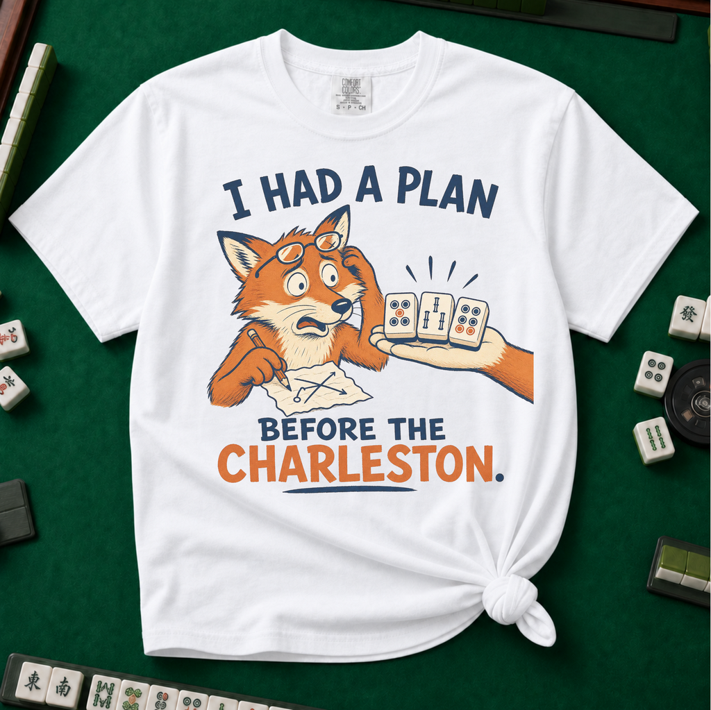 I Had A Plan Before The Charleston T-Shirt in White, knotted flat lay on a green mahjong mat - a stressed cartoon fox with glasses and a strategy sketch being handed three mahjong tiles, with the words "I HAD A PLAN BEFORE THE CHARLESTON."