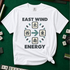 East Wind Energy T-Shirt in White, knotted flat lay on a green mahjong mat - the four mahjong wind tiles arranged in a compass circle - North on top, West left, East right, South below - with a big teal arrow pointing East, between "EAST WIND" and "ENERGY" in charcoal block letters