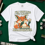 I'm Trying To Look Disappointed T-Shirt in White, knotted flat lay on a green mahjong mat - smug retro fox holding up a joker tile, hiding a grin behind one paw, tile rack in front - "I'M TRYING TO LOOK DISAPPOINTED." in cream collegiate letters
