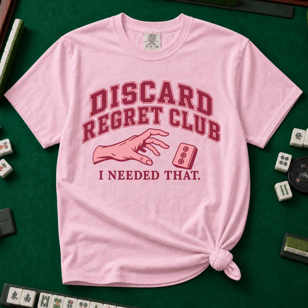 Discard Regret Club I Needed That T-Shirt in Blossom, knotted flat lay on a green mahjong mat - burgundy varsity letters "DISCARD REGRET CLUB" over a pink hand reaching back for a pink dot tile it just discarded - "I NEEDED THAT."