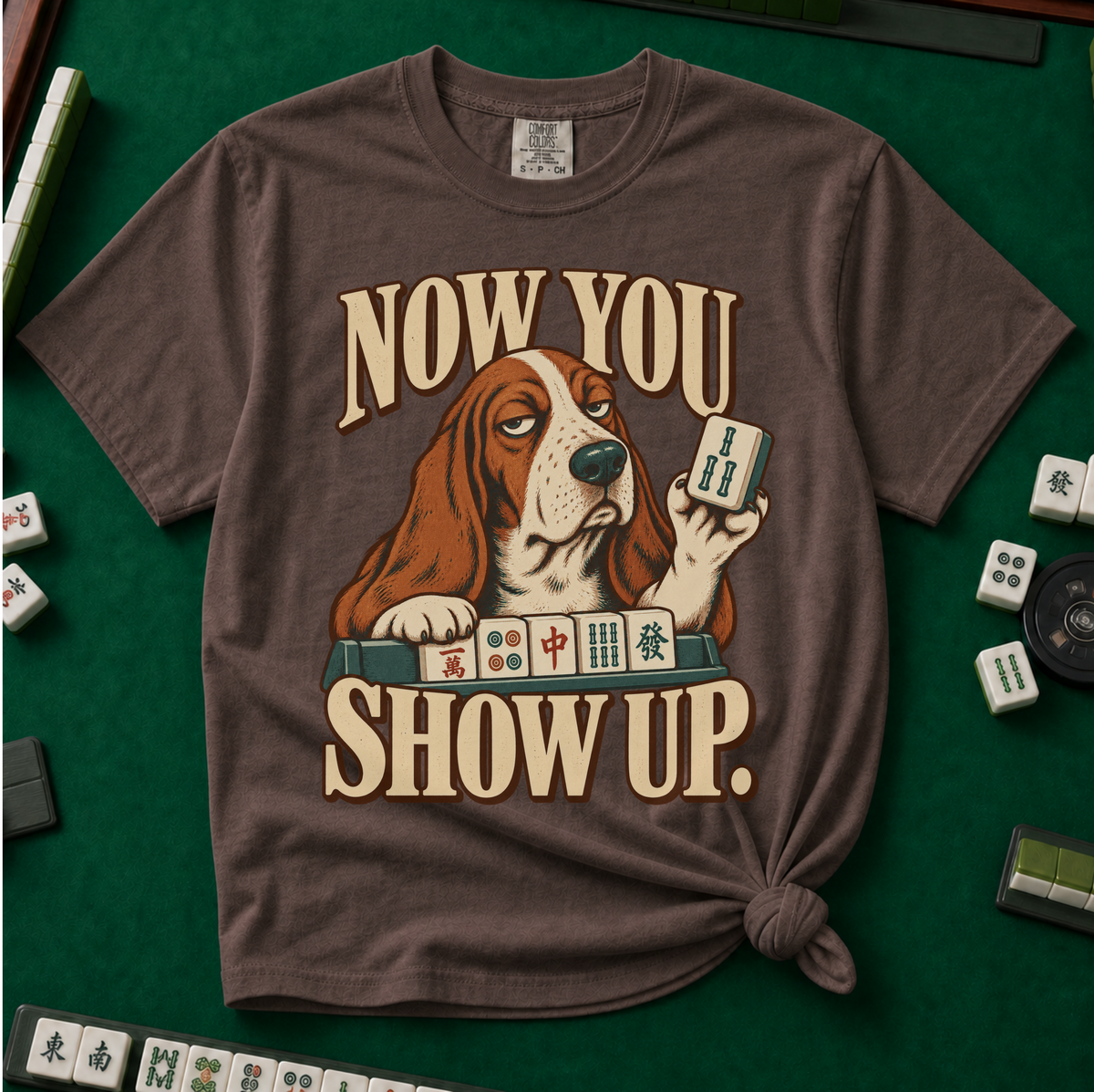 Now You Show Up Shirt in Espresso - knotted tee on a green mahjong mat with scattered tiles, printed with a basset hound peeking over a row of mahjong tiles and the words Now You Show Up