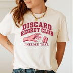 Woman wearing the Discard Regret Club I Needed That T-Shirt in Ivory - burgundy varsity letters "DISCARD REGRET CLUB" over a pink hand reaching back for a pink dot tile it just discarded - "I NEEDED THAT."