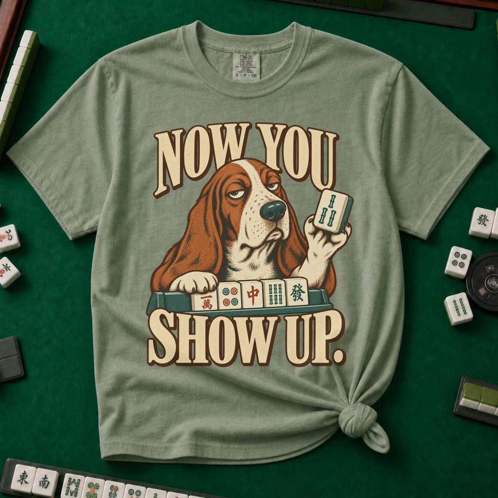 Now You Show Up Shirt in Moss - knotted tee on a green mahjong mat with scattered tiles, printed with a basset hound peeking over a row of mahjong tiles and the words Now You Show Up