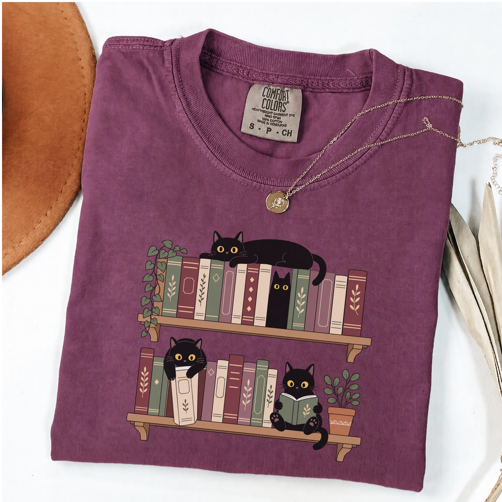 Berry Comfort Colors book-lover shirt featuring black cats among colourful bookshelves
